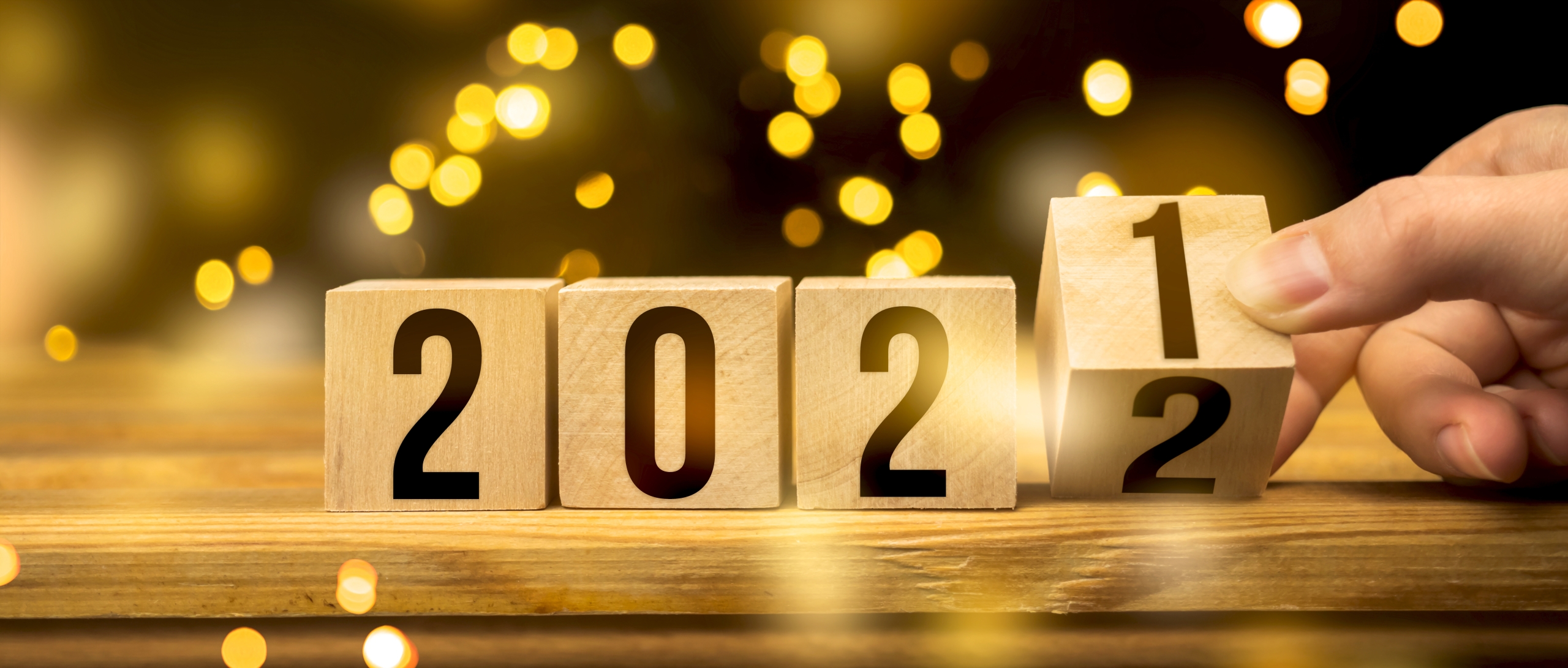 Dal 2021 al 2022, Happy New Year concept. Mano che cambia il numero dell'anno girando un blocco di legno, con lucine di sottofondo